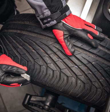 Mechanic in a garage with red and black gloves handling a tire