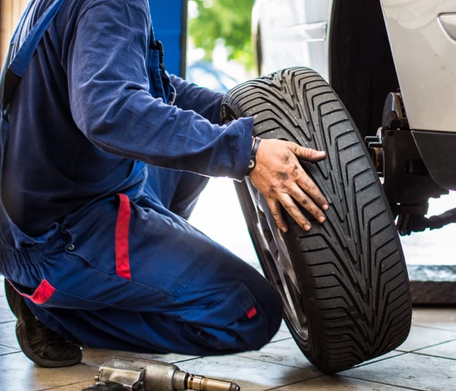 Man in a mechanic's uniform holding an inflated tire inside of a garage