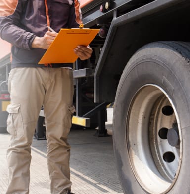 Mechanic with clipboard performing maintenance on a large vehicle tire